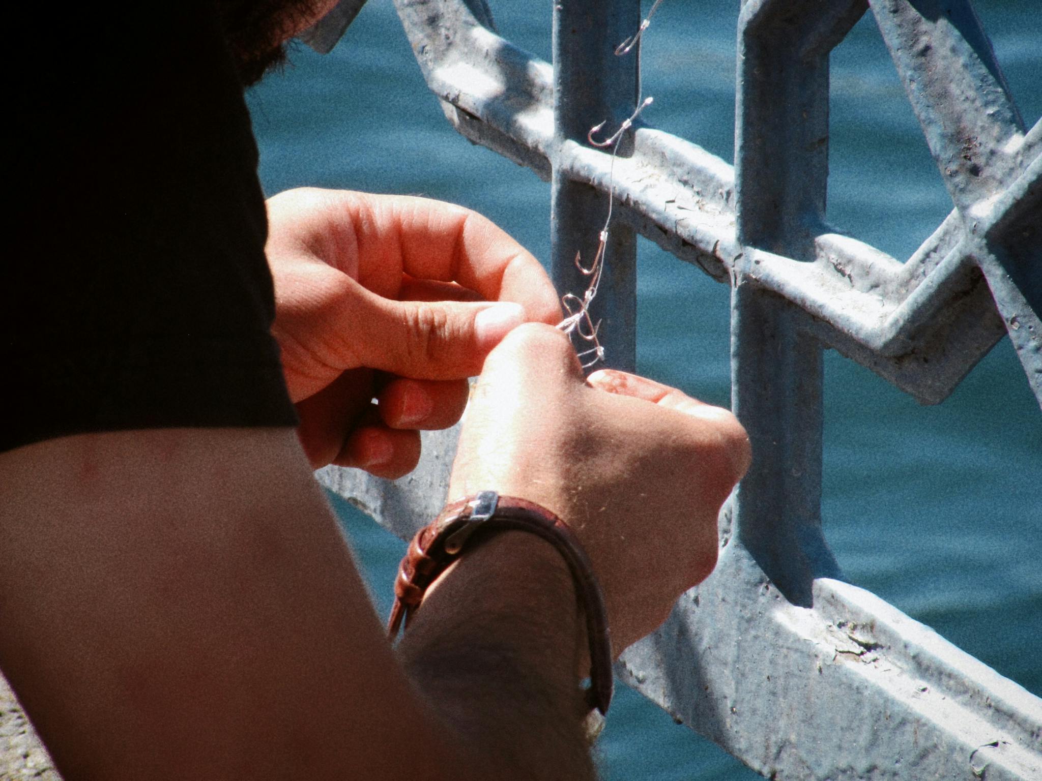 Close-up of a person setting up a fishing line by a waterfront railing.